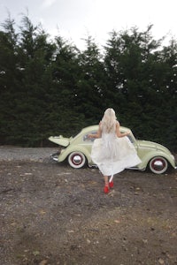a woman in a white dress is running in front of a car